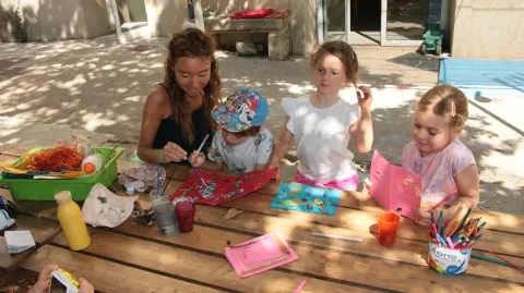 Une animatrice colle avec un enfant un éléments naturel et deux autres enfants nous montrent leurs œuvres