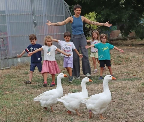 Un groupe d'enfants et leur animatrice ouvent les bras derrière trois oies