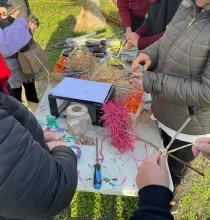 une table avec du rafia, de la corde, des perles divers outils et des adultes autour qui se servent 