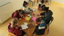 Cinq enfants et leur animateur plient du papier sur une table