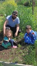 Deux enfants et leur animateur sont devant des plants de tomate au jardin