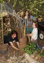 2 enfants et leur animatrice mettent de la boue sur une struture en métal