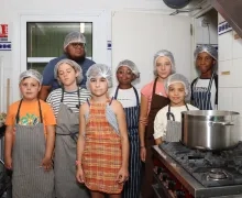 Un groupe d'enfants et leur animateur sont en cuisine à côté d'une grosse marmite