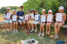 Un groupe d'enfants et leur animateur sont assis sur des bancs et montrent des dessins