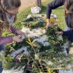 Deux adultes créent une couronne de feuille, il y a différentes feuilles, branches et fleurs