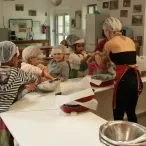 Six enfants avec leurs charlottes sur la tête pétrissent la pâte avec leur animatrice pour faire les focaccia dans la cuisine pédagogique