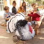 un groupe d'enfants et leur animatrice sont installés à une table avec un dindon devant